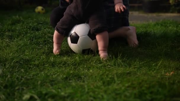 ハッピーベビーは緑の草の上にサッカーブラックホワイトクラシックボールで座っています。裏庭で屋外で遊ぶ愛らしい幼児の赤ちゃん。親を持つ小さな子供。サッカー,選手権,スポーツコンセプト — ストック動画