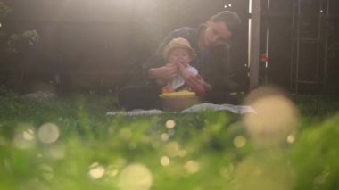Mutlu Genç Neşeli Anne Yeşil Çimlerde Bebek Yiyen Meyveler Tutuyor. Sevimli Anne Bebek Arka Bahçe Bahçesinde Dışarıda Sevgiyle Oynuyor. Ailesi olan küçük çocuk. Aile, Doğa, Ekoloji Kavramı