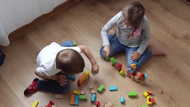 Deux enfants d'âge préscolaire heureux garçons fille dans la salle de jeu. Enfants du même âge jouent avec des jouets en bois à la construction de la maison. Le bébé a passé du temps à la maison. Enfance, Parentalité, Concept d'amitié — Video