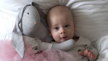 Yakın plan Mutlu neşeli çocuk 6 aylık. Yeni doğan çocuk, beyaz yumuşak yatakta banyo sonrası kameraya bakıyor. Bebek oyuncakla yatmadan önce uyandı. Çocukluk, annelik, aile, bebek konsepti