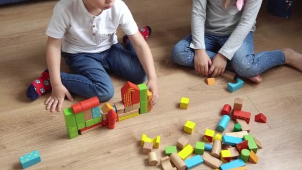 Deux enfants d'âge préscolaire heureux garçons fille dans la salle de jeu. Enfants du même âge jouent avec des jouets en bois à la construction de la maison. Le bébé a passé du temps à la maison. Enfance, Parentalité, Concept d'amitié — Video