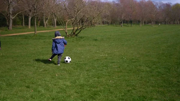 Glückliche Familie von Kindern, die Spaß im Spring Park haben. Kleiner Kinderlauf. Child Boy dribbelt schwarz weiß klassischen Fußballball auf grünem Gras. Menschen, die Fußball spielen. Kindheit, Sport, Meisterschaftskonzept — Stockfoto