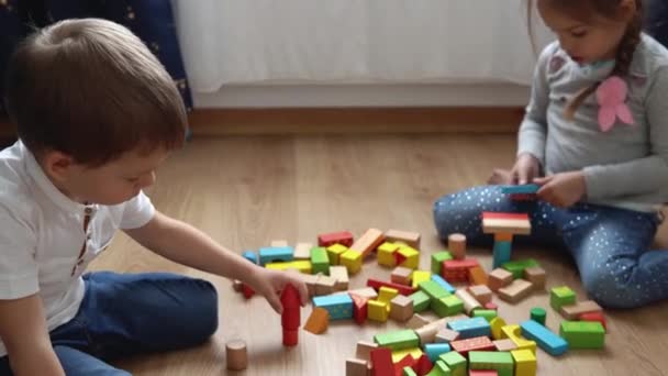 Twee gelukkige kleuterschool broers en zussen kinderen jongen meisje in speelkamer. Kinderen van dezelfde leeftijd spelen met houten speelgoed thuis bouwen van de bouw. De baby is thuis geweest. Jeugd, Ouderschap, Vriendschap Concept — Stockvideo