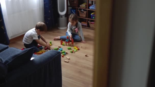 两个快乐的幼稚园弟妹在游戏室。同年龄的孩子在家庭建设中玩木制玩具。婴儿有很多时间待在家里。童年、父母、友谊概念 — 图库视频影像