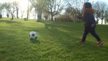 Mutlu çocuk ailesi bahar parkında eğleniyor. Küçük Çocuk Koş. Çocuk Çocuk Yeşil Çimende Siyah Beyaz Klasik Futbol Topu Sürüyor. İnsanlar futbol oynuyor. Çocukluk, Spor, Şampiyonluk Konsepti