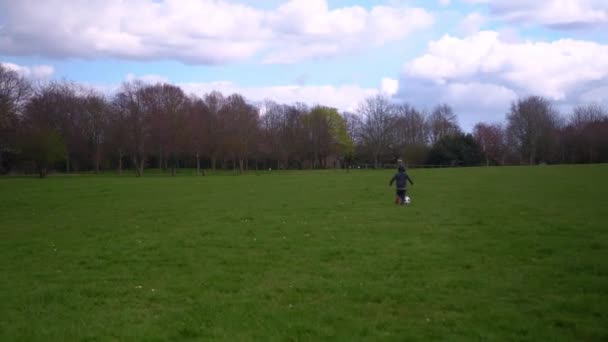 Glückliche Familie von Kindern, die Spaß im Spring Park haben. Kleiner Kinderlauf. Child Boy dribbelt schwarz weiß klassischen Fußballball auf grünem Gras. Menschen, die Fußball spielen. Kindheit, Sport, Meisterschaftskonzept — Stockvideo