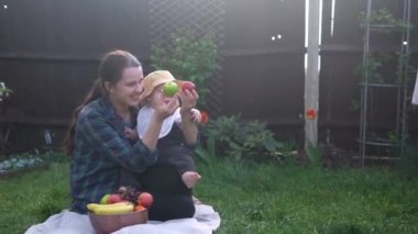 Mutlu Genç Neşeli Anne Yeşil Çimlerde Bebek Yiyen Meyveler Tutuyor. Sevimli Anne Bebek Arka Bahçe Bahçesinde Dışarıda Sevgiyle Oynuyor. Ailesi olan küçük çocuk. Aile, Doğa, Ekoloji Kavramı