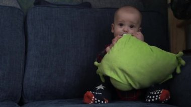 Mutlu gülümseyen bebek, mavi koltukta oturup oyuncaklarla oynayıp kameraya bakarken meme emer. Aktif 7 aylık, yeni doğmuş tatlı çocuk evde yumuşak oyuncakları keşfederken eğlenir. Çocukluk, annelik.