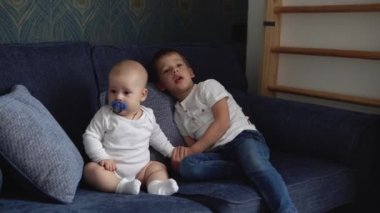 Two Happy Siblings Children Boys Brothers In Playing Room. Kids Infand and Preschool Play On Comfortable Sofa Watching TV. Baby Have Spent Time At Home. Childhood, Parenthood, Friendship Concept