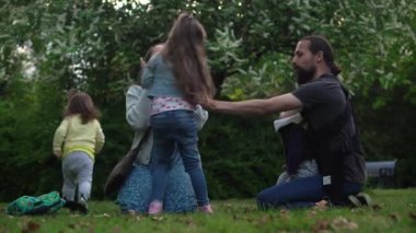 Mutlu aile annesi baba üç küçük kardeş çocuklar bahçe parkında yaz tatilinin tadını çıkarırken eğleniyor. Gülümseyen ebeveynler çocuklar akşam günbatımında birlikte vakit geçiriyorlar.