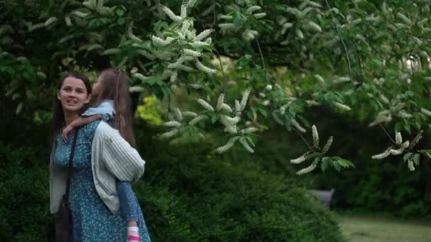 Happy family mother with two Daughters little siblings kids have fun sniffing flowers on trees enjoying summer holidays in garden park. Smiling parents children spending leisure time together sunset — Vídeos de Stock