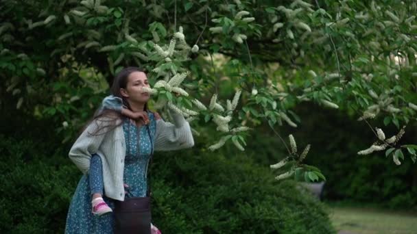 Happy family mother with Daughter little kid have fun sniffing flowers on trees enjoying summer holidays in garden park. Smiling children spending leisure time together sunset Motherhod Mother Day — Wideo stockowe