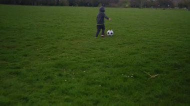 Mutlu çocuk ailesi bahar parkında eğleniyor. Küçük Çocuk Koş. Çocuk Çocuk Yeşil Çimende Siyah Beyaz Klasik Futbol Topu Sürüyor. İnsanlar futbol oynuyor. Çocukluk, Spor, Şampiyonluk Konsepti
