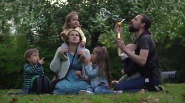 Mutlu aile annesi baba üç küçük kardeş çocuklar bahçe parkında yaz tatilinin tadını çıkarırken eğleniyor. Gülümseyen ebeveynler çocuklar akşam günbatımında birlikte vakit geçiriyorlar.