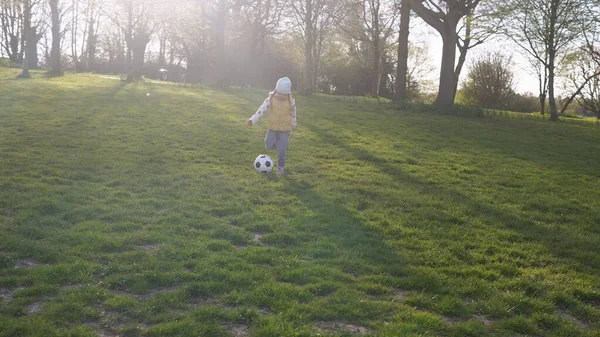 春の公園で楽しい子供たちの幸せな家族。リトル・キッド・ラン。子供の女の子は緑の草の上にブラックホワイトクラシックサッカーボールをドリブル。サッカーをしている。子供時代,スポーツ,選手権のコンセプト — ストック写真