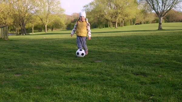 Happy Family Of Children Having Fun In Spring Park. Little Kid Run. Child Girl Dribbles Black White Classic Soccer Ball On Green Grass. People Playing Football. Childhood, Sport, Championship Concept