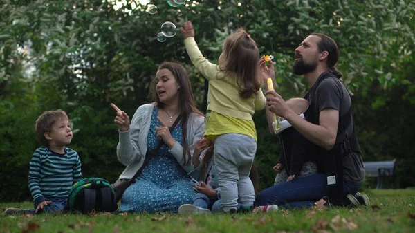 Happy family mother Father Three four Baby little siblings kids have fun blowing bubbles enjoying summer holidays in garden park. Smiling parents children spending leisure time together evening sunset — Stok fotoğraf