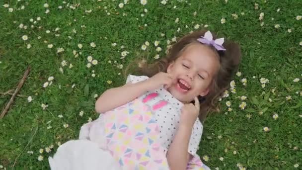 Parktaki Yeşil Çimlerin Üzerinde Başı Fiyonklu Küçük Mutlu Kız Çocuğu — Stok video