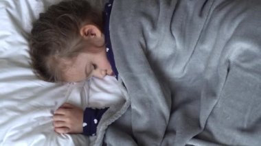 Otantik, şirin, tatlı, rahat beyaz ve gri yatakta uyuyan bir kız. Güzel, yorgun çocuk, dinlenme zamanı, dinlenme zamanı. Beşikteki çocuk. Bakım, Çocukluk, Ebeveynlik, Yaşam Konsepti.