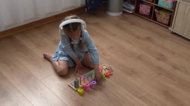 Renkli ahşap oyuncaklarla oynayan Dişsiz Mutlu Anaokulu Kızı. Çocuklar evde numara öğreterek saymayı öğrenirler. Büyük beyaz kulaklıkla müzik dinleyen çocuk. Çocukluk, Eğitim.