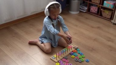 Renkli ahşap oyuncaklarla oynayan Dişsiz Mutlu Anaokulu Kızı. Çocuklar evde numara öğreterek saymayı öğrenirler. Büyük beyaz kulaklıkla müzik dinleyen çocuk. Çocukluk, Eğitim.