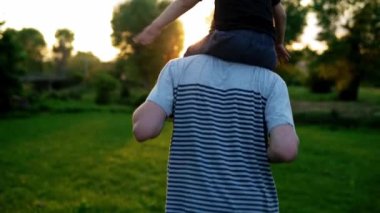 Yaz, tatil, doğa, mutlu aile, çocukluk, babalık, baba günü - küçük bir anaokulu çocuğuyla çocuk çocuk kanat çırpmaca oynuyor çocuklar günbatımında parktaki çayırda omuzlarına oturup eğleniyor.