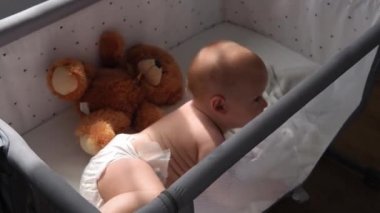 Yakından bakınca şirin çocuk bezi 10 aylık yeni doğan çocuk kameraya bakıyor ve beşiğine ilk adım olarak bacaklarının üzerinde sürünüyor. Bebek, yatmadan önce uyanma zamanı. Çocukluk, Annelik, Aile, Bebek Konsepti