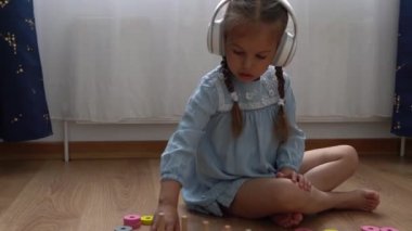 Renkli ahşap oyuncaklarla oynayan Dişsiz Mutlu Anaokulu Kızı. Çocuklar evde numara öğreterek saymayı öğrenirler. Büyük beyaz kulaklıkla müzik dinleyen çocuk. Çocukluk, Eğitim.