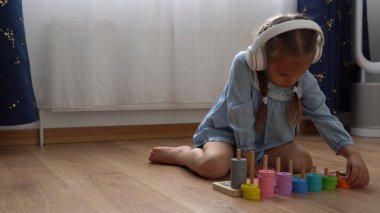 Renkli ahşap oyuncaklarla oynayan Dişsiz Mutlu Anaokulu Kızı. Çocuklar evde numara öğreterek saymayı öğrenirler. Büyük beyaz kulaklıkla müzik dinleyen çocuk. Çocukluk, Eğitim.