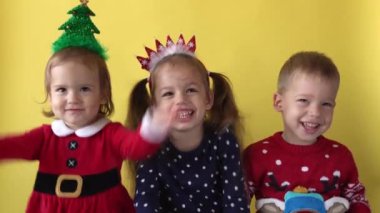 Sevimli, mutlu, neşeli, 3 kardeş arkadaş, bebek kız ve Noel Baba kılığındaki çocuk, sarı arka plandaki kameraya bakıp gülümsüyor. Çocuklar Noel 'i kutluyor. Çocuk Yılbaşını Eğlenerek Geçiriyor