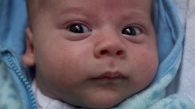 Kameradaki bebeğe bak. Yakın çekim. bebek, çocukluk, ebeveyn sevgisi, duygusal konsept - kahverengi gözlü tombul bebeğin sevimli gülen yüzü yumuşak mavi ceketli bebek uyanık yatağında yatıp etrafına bakıyor.
