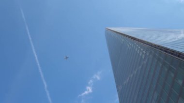 Londra 'daki gökdelenlerin iş merkezinin üzerinden geçen uçak. Öğleden sonra bulutlu, mavi gökyüzünde uçan bir uçakla yüksek binaların alt görüntüsü. Hava Taşımacılığı, Seyahat, Meslek kavramı