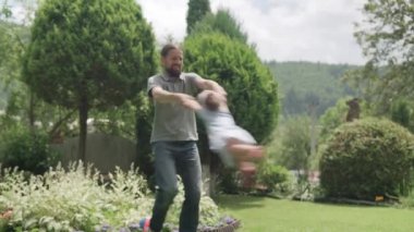 Neşeli Aile Komik Babası sakallı Çocuklar Kollar Arasında Sallanıyor. Baba, anaokulu kızı ve oğlu güneşli yaz gününde Idyllic Banliyö Evinin arka bahçesinde oyun oynuyorlar..