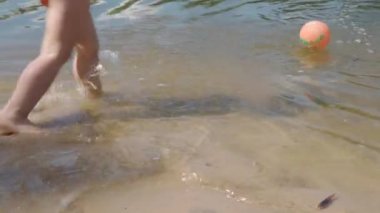 İki küçük neşeli çocuk köyde nehirde top oynarken suda yüzüyor. Sıcak yaz sıcağında çocuklarla plajda tatil. Plaj güneşli güneş banyosu, eğlence, bulanık geçmiş çocukluk kavramları..