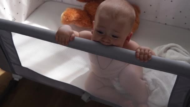 特写可爱的孩子10个月大的新生儿早上在白色软婴儿床里看相机 活泼的婴儿脸咬牙切齿的一切 牙龈痛 牙龈痛童年 — 图库视频影像