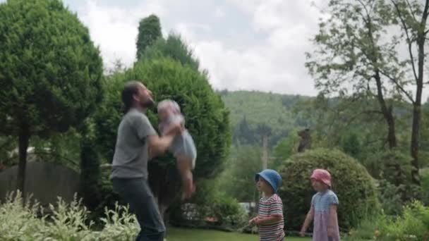 快乐的家庭有趣的年轻爸爸 带着胡子把孩子们抱得高高的 阳光明媚的夏日 女儿和儿子在Idyllic Suburban House后院草坪玩乐游戏 — 图库视频影像