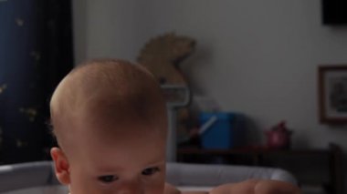 Yakından bakınca şirin çocuk bezi 10 aylık yeni doğan çocuk kameraya bakıyor ve beşiğine ilk adım olarak bacaklarının üzerinde sürünüyor. Bebek, yatmadan önce uyanma zamanı. Çocukluk, Annelik, Aile, Bebek Konsepti