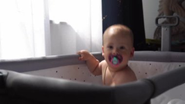 Yakından bakınca şirin çocuk bezi 10 aylık yeni doğan çocuk kameraya bakıyor ve beşiğine ilk adım olarak bacaklarının üzerinde sürünüyor. Bebek, yatmadan önce uyanma zamanı. Çocukluk, Annelik, Aile, Bebek Konsepti