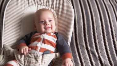 Kameradaki bebeğe bak. Bebek, çocukluk, aile sevgisi. Çizgili pijamayla yeni doğmuş sevimli gülümseyen yüz uyanmış ve evdeki yumuşak sandalyeye uzanmış etrafına bakıyor. Mutlu çocuğun neşeli yaşam tarzı.