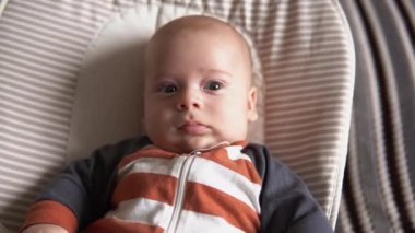 Kameradaki bebeğe bak. Bebek, çocukluk, aile sevgisi. Çizgili pijamayla yeni doğmuş sevimli gülümseyen yüz uyanmış ve evdeki yumuşak sandalyeye uzanmış etrafına bakıyor. Mutlu çocuğun neşeli yaşam tarzı.