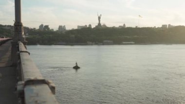 Gündoğumunda Dnipro nehrinde okyanusu hareket ettiren üst hava manzaralı bir balıkçı teknesi. Kiev şehrindeki köprülerin anavatanının manzara heykeli. Su taşımacılığı, seyahat, yaz, dinlenme, rezervuarlar.