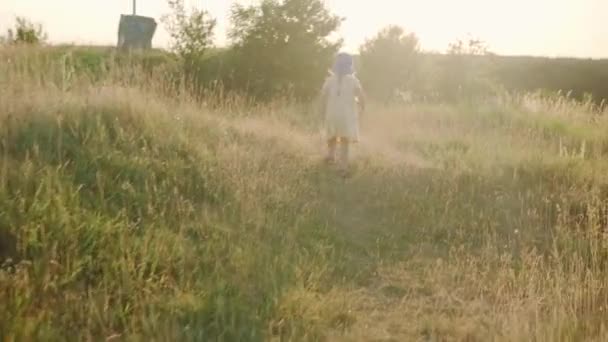 可爱的学龄前小女孩穿着黄色衣服 日落前爬上了高高的草地上的小径 在野外草地上散步的孩子 在山上快乐的孩子 生活方式 夏天概念 — 图库视频影像