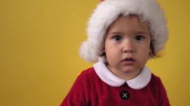 Duyguyu kapat. Mutlu, neşeli, tombul, bebek bebek Noel Baba kostümlü, sarı arka plandaki kameraya bakıyor. Çocuk Noel Sahnesi Oynuyor Doğum gününü kutluyor. Çocuk Yılbaşını Eğlenerek Geçiriyor