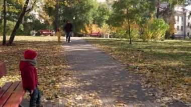 Küçük şirin okul öncesi küçük kardeş oğlan ve babası Sonbahar Parkı 'nda güneşli bir günde el ele tutuşuyorlar. Sepette Düşen Yapraklar Soğuk Hava Kamerasına Bakar. Çocukluk, Mutlu Aile, Sonbahar Konsepti.