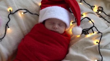 Yeni doğan bebeğin ilk portresi beyaz çelenk arka planında kırmızı beze sarılı, Noel Baba şapkalı komik uyuyan bebek. Mutlu Noeller, Mutlu yıllar, Bebek, Çocukluk, Kış Konsepti