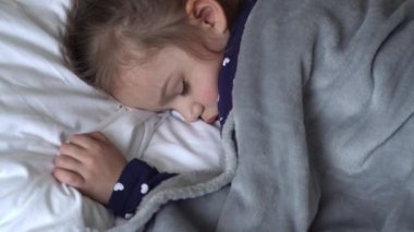 Otantik, şirin, tatlı, rahat beyaz ve gri yatakta uyuyan bir kız. Güzel, yorgun çocuk, dinlenme zamanı, dinlenme zamanı. Beşikteki çocuk. Bakım, Çocukluk, Ebeveynlik, Yaşam Konsepti.