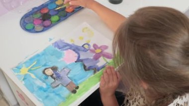 Talented Creative Child Girl Female Artist Draws with Her Hands on Paper, Using Fingers Paints Brush Creates Colorful, Kid Drawing on table at Home. Painter Creating Abstract Modern Art. Childhood.
