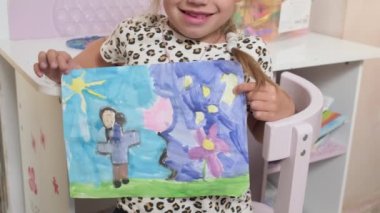 Talented Creative Child Girl Female Artist Draws Ranbow Mother summer on Paper, Child showing her work.Creates Colorful, Kid Drawing on table at Home. Painter Creating Abstract Modern Art. Childhood.