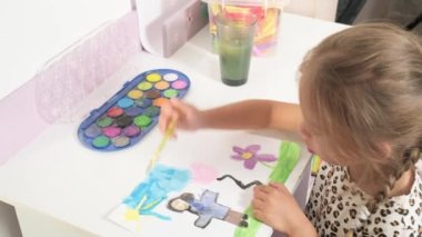 Talented Creative Child Girl Female Artist Draws with Her Hands on Paper, Using Fingers Paints Brush Creates Colorful, Kid Drawing on table at Home. Painter Creating Abstract Modern Art. Childhood.