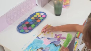 Talented Creative Child Girl Female Artist Draws with Her Hands on Paper, Using Fingers Paints Brush Creates Colorful, Kid Drawing on table at Home. Painter Creating Abstract Modern Art. Childhood.